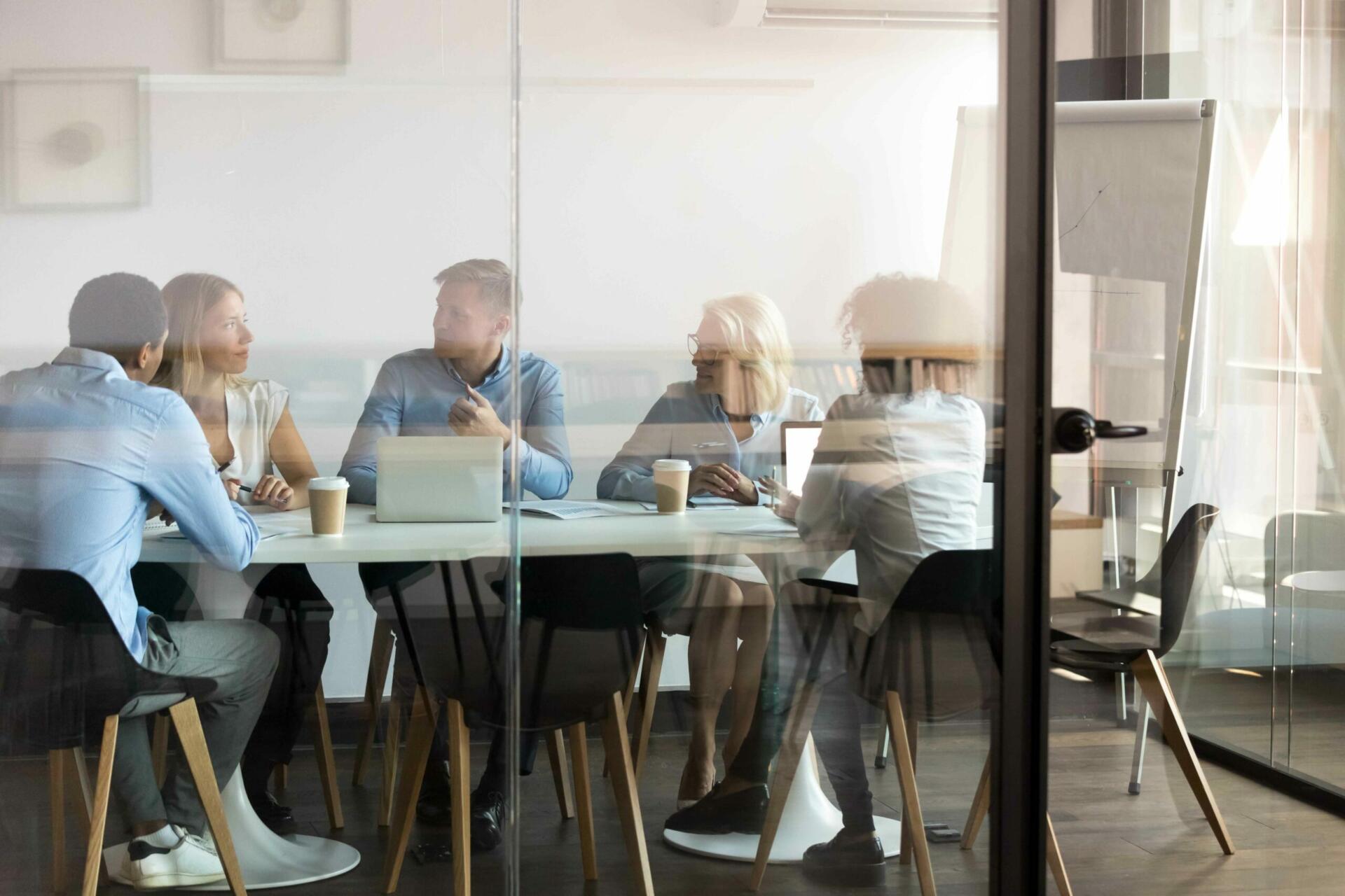 Colleagues meeting around a table in a glass-walled office.